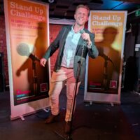 Rob Spence stands on a stage holding a microphone.