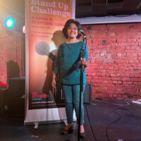 Trusha Lakhani stands on stage behind a microphone.